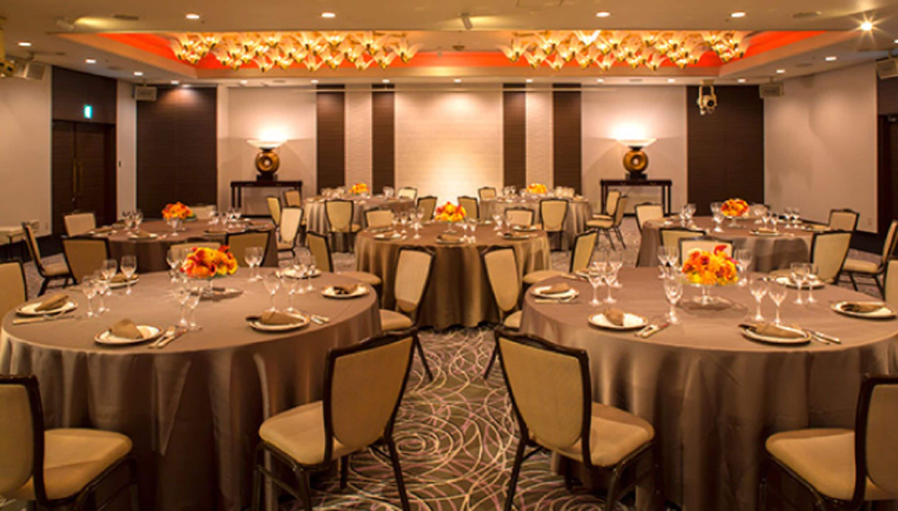 Un salón de conferencias con mesas redondas, sillas y centros de mesa con flores.