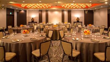 Un salón de conferencias con mesas redondas, sillas y centros de mesa con flores.