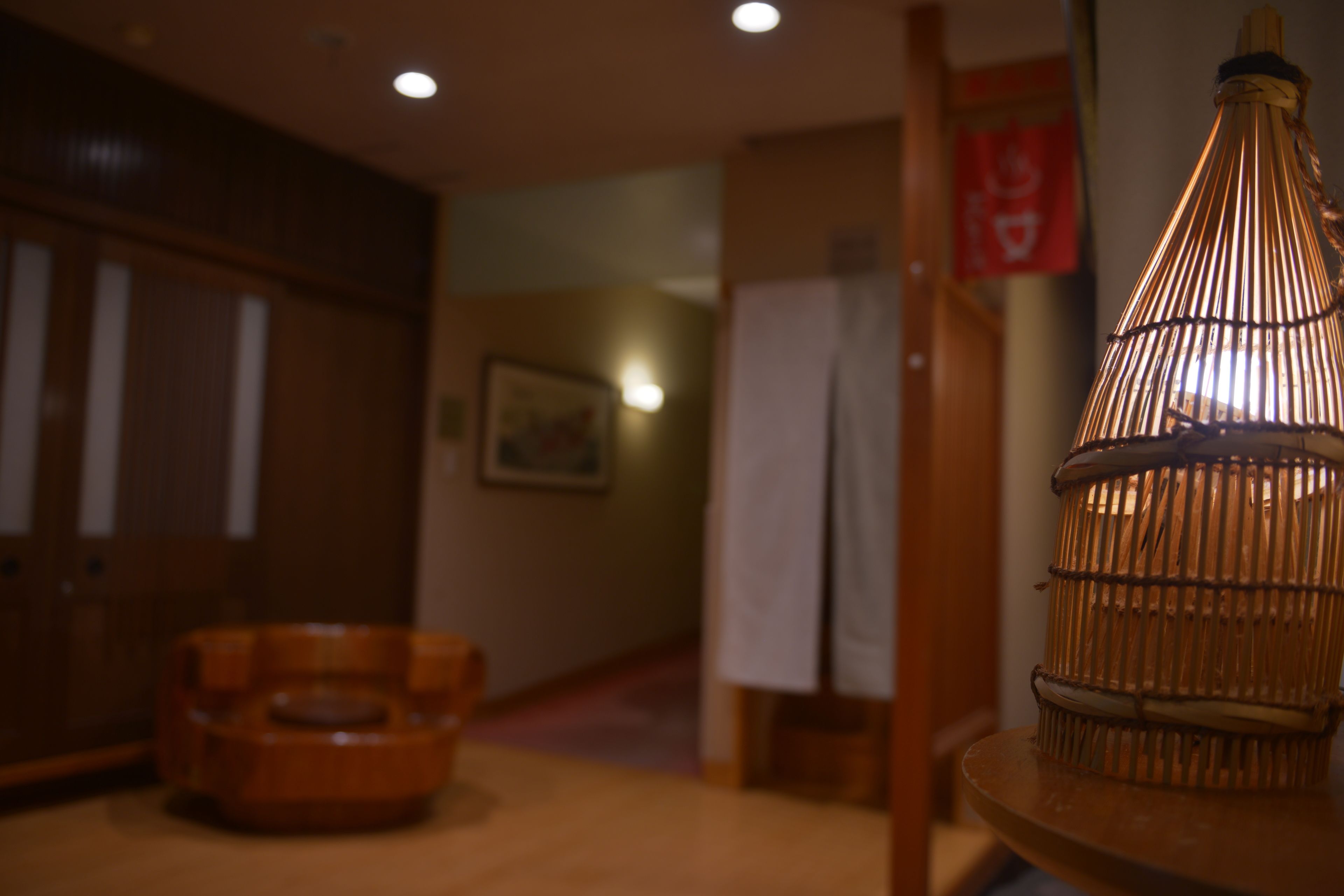 A room with a wooden floor, a wicker chair, a hanging light fixture, and a wooden cabinet.