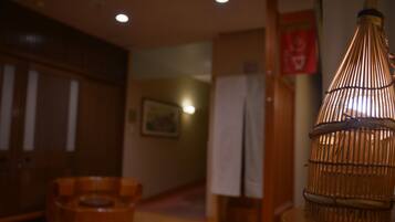 A room with a wooden floor, a wicker chair, a hanging light fixture, and a wooden cabinet.