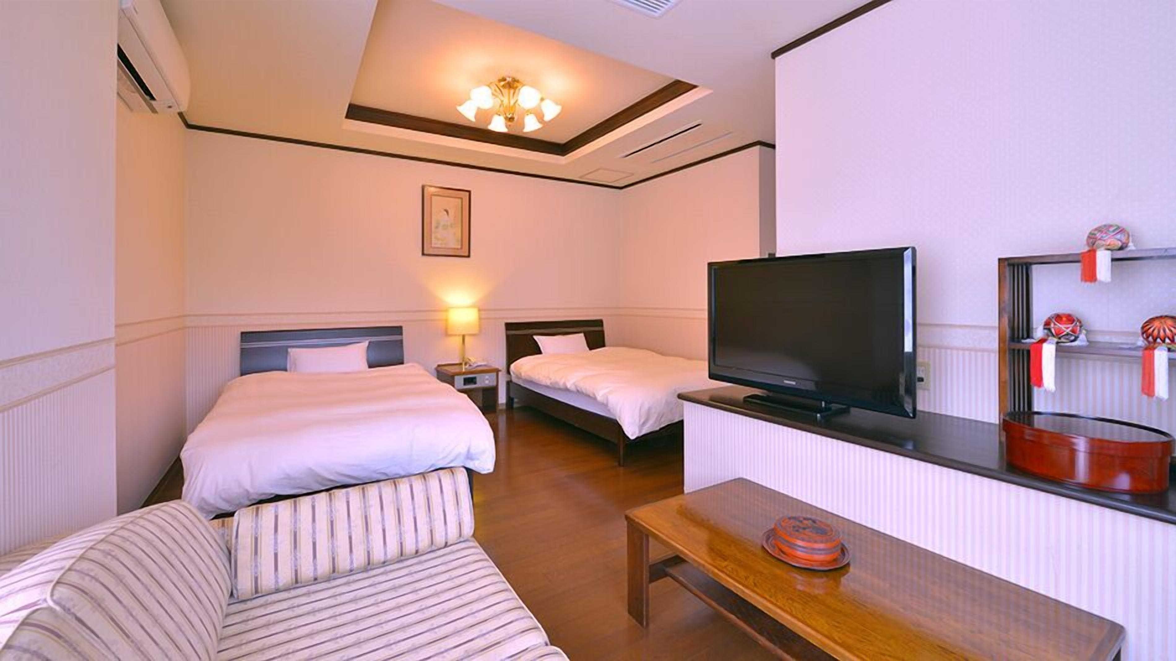 Une chambre d’hôtel avec deux lits, une télévision, une table en bois et une petite étagère ornée d’objets décoratifs.