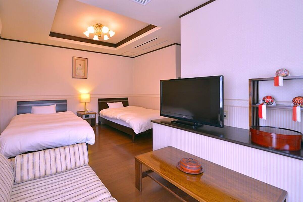 Ein Hotelzimmer mit zwei Betten, einem Fernseher, einem Holztisch und einem kleinen Regal mit Dekoration.