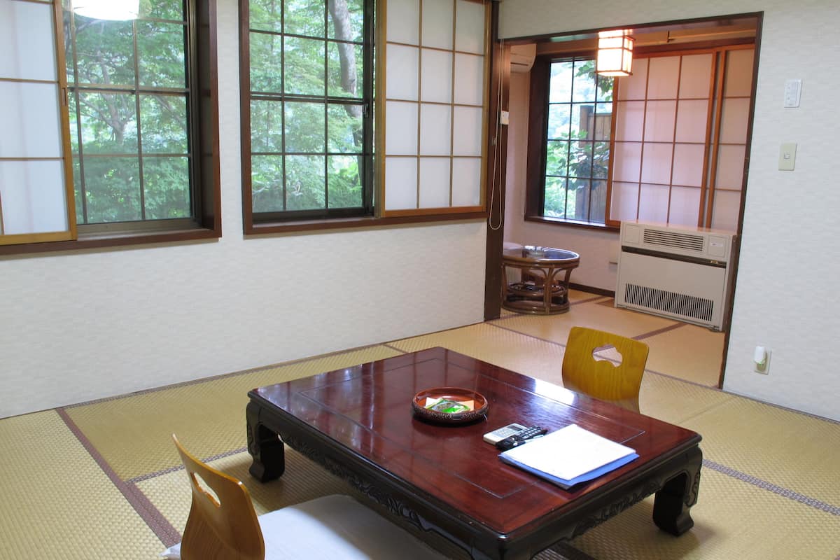 Ein traditioneller japanischer Raum mit Tatami-Bodenbelag, einem niedrigen Holztisch und einer Schiebetür zum Garten.