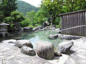 A traditional Japanese onsen with stone steps leading into a clear hot spring surrounded by rocks and greenery.