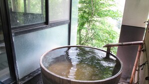 Een groot houten vat gevuld met water, geplaatst binnen, in de buurt van een raam met uitzicht op groen.