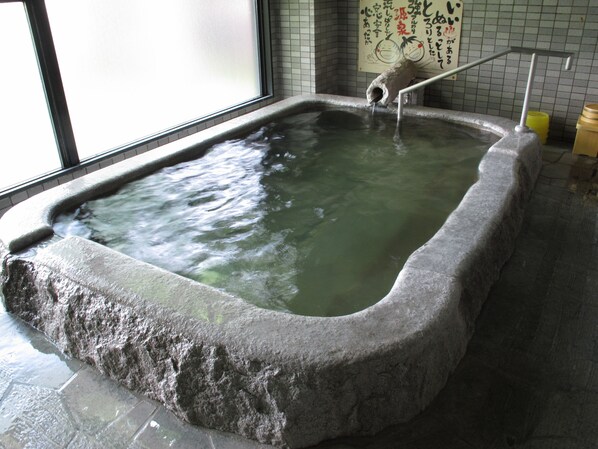 A stone hot spring bath with a metal railing and a wooden bucket.