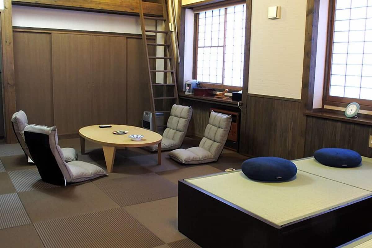 Une pièce avec un sol recouvert de tatamis, une petite table basse, deux chaises et un futon servant de lit.