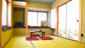 Una habitación con suelo de tatami, una cama futón, una mesita con un marco de fotos y puertas correderas.