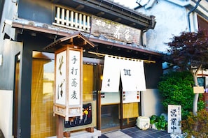 A traditional Japanese building with a wooden facade, a signboard with Japanese characters, and a small shrine-like structure in front.