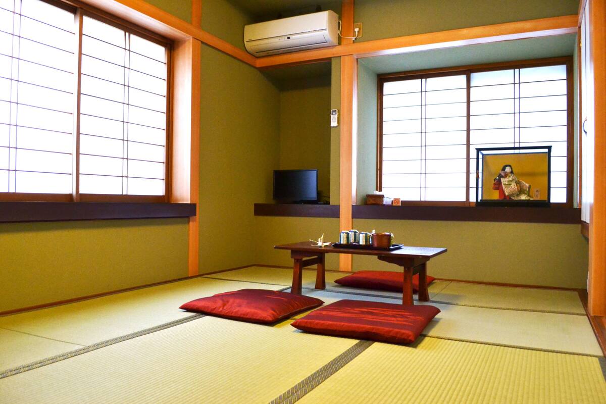 Um quarto japonês tradicional com tatames, uma mesa baixa com almofadas e uma televisão.