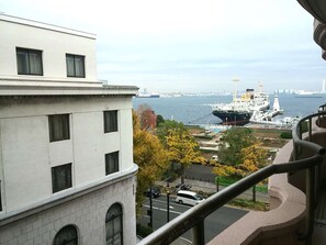 Vista desde un balcón sobre un muelle con un barco grande amarrado, edificios y follaje otoñal.