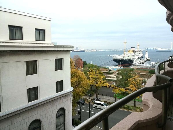 Vista desde un balcón sobre un muelle con un barco grande amarrado, edificios y follaje otoñal.