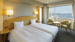 Ein Hotelzimmer mit einem großen Bett, zwei Nachttischen, einem Sessel und einem kleinen Tisch, mit Blick auf das Meer.