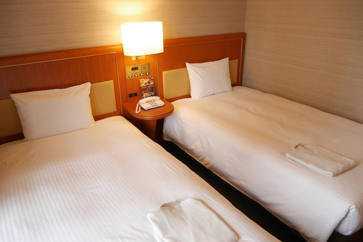 Une chambre d’hôtel avec deux lits simples, une table de chevet avec une lampe, un téléphone et une serviette pliée.