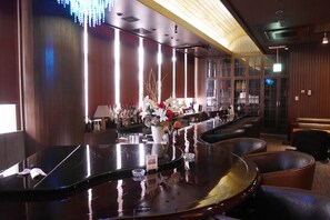 A bar area with a polished bar counter, a vase of flowers, and leather seating.