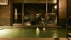 A nighttime view of a swimming pool area with a glass door leading to a garden. - Yamadaya Ryokan (Kyoto)