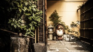 A stone pathway leading to a traditional Japanese entrance with a wooden gate, a stone lantern, and a statue. - Yamadaya Ryokan (Kyoto)