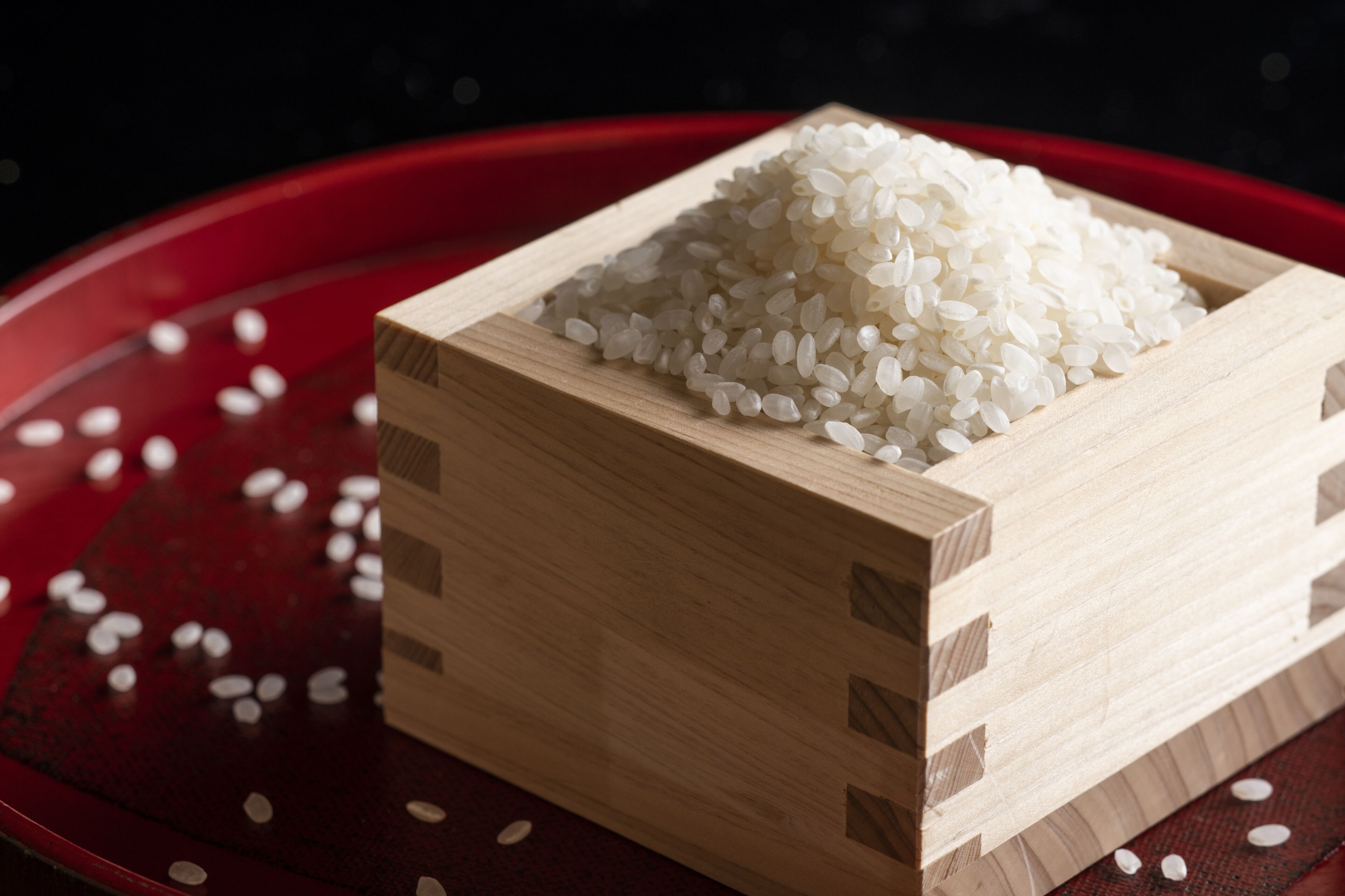 A wooden box filled with white rice on a red surface.
