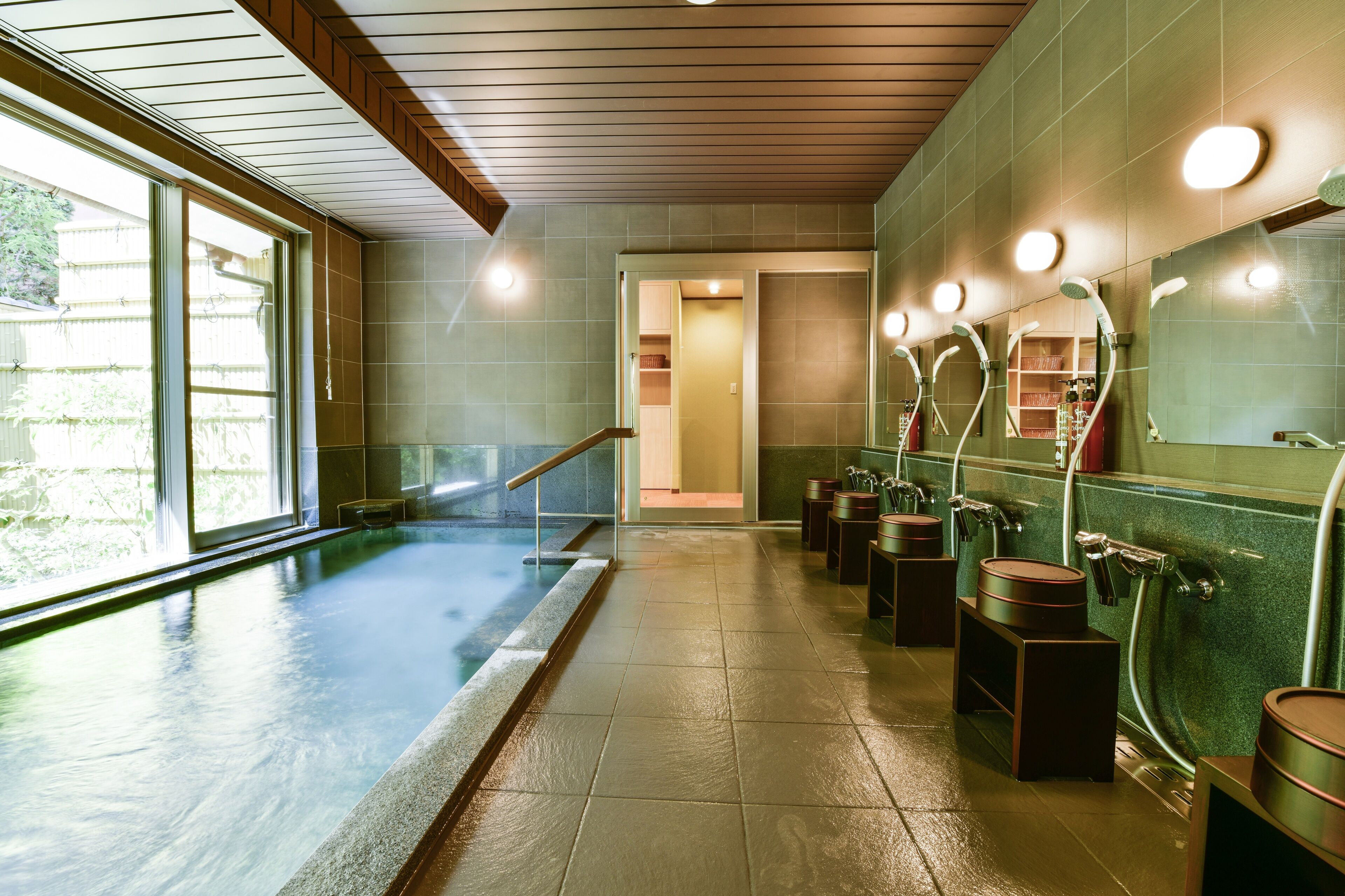 A spa area with a large indoor pool, multiple showerheads, and a glass door leading to a changing room.
