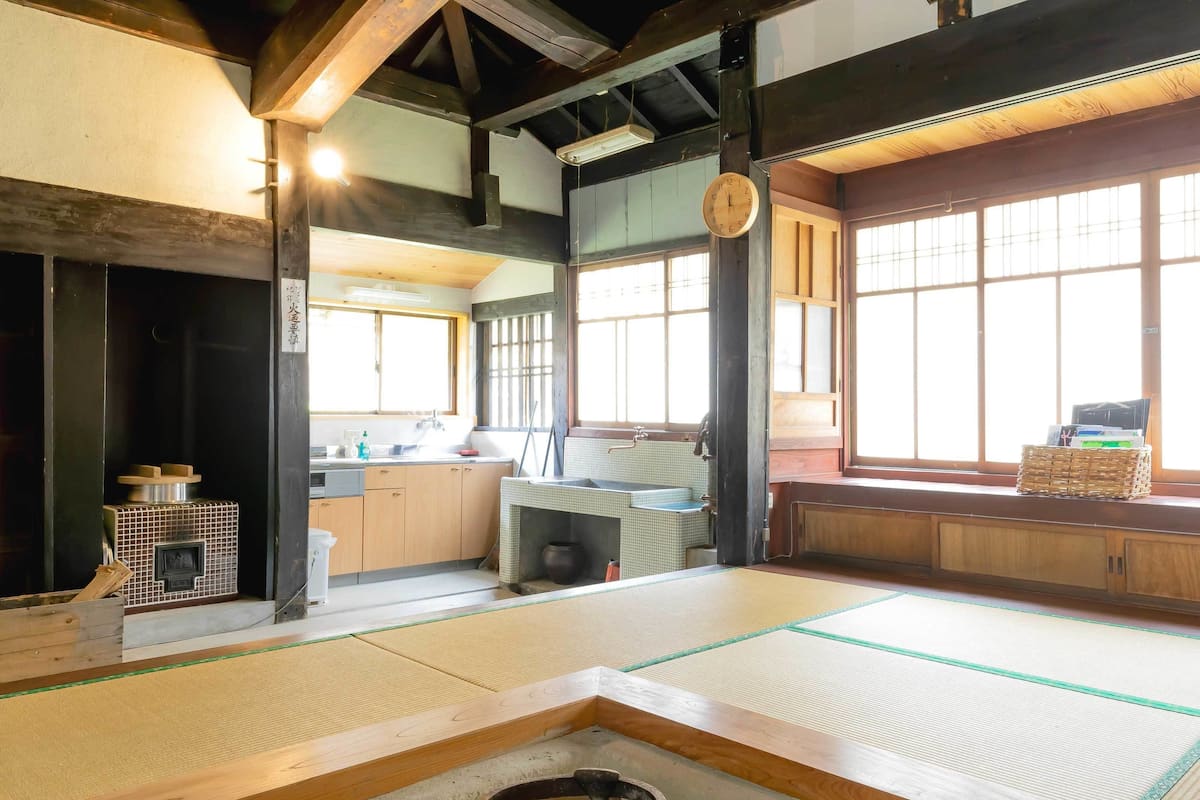Una habitación japonesa tradicional con suelo de tatami, una mesa baja de tatami, un armario de madera, un lavabo y una ventana con vistas.