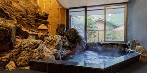 A hot spring bath with a rocky interior and a view of a traditional house through a large window. - Kigusuriya (Nantan)