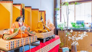Una habitación japonesa tradicional con tatamis, una mesa baja cubierta con un paño rojo y una ventana con vistas a la vegetación.