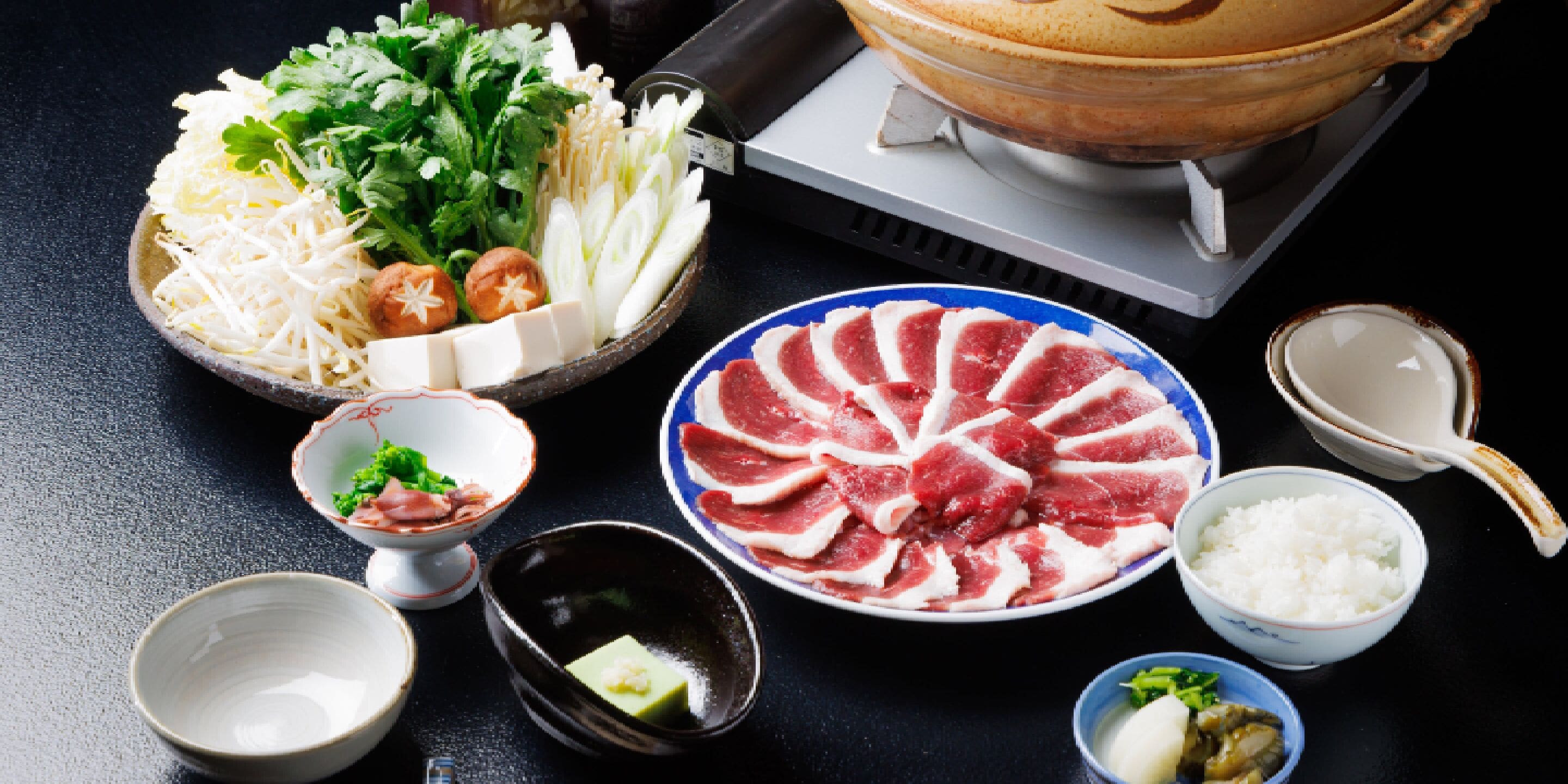 A variety of food items including sliced meat, vegetables, and rice, arranged on a dark surface.