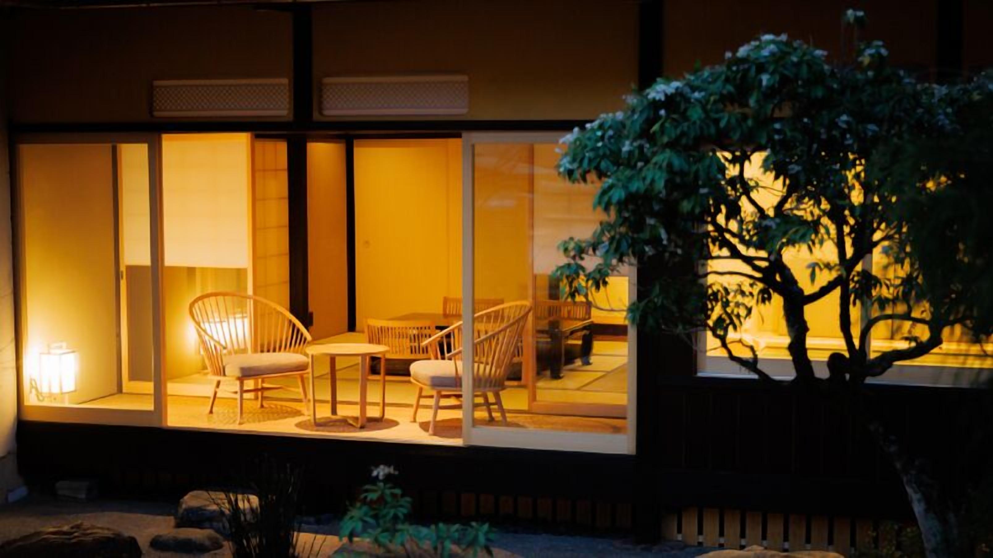 A well-lit outdoor seating area with chairs and a table, surrounded by large windows.