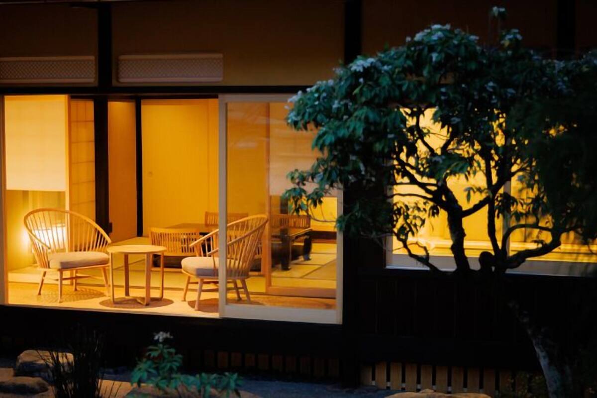 Un espacio al aire libre bien iluminado con sillas y una mesa, rodeado de amplias ventanas.