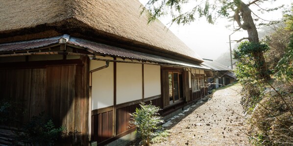 A traditional Japanese building with a thatched roof, wooden walls, and a narrow stone pathway leading to it.