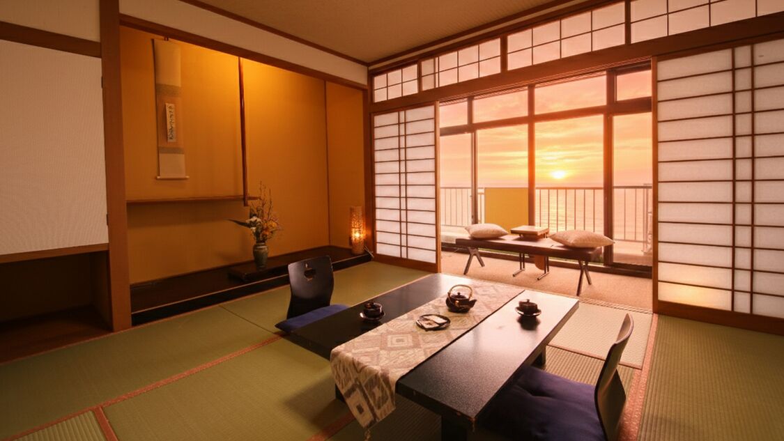 Een traditionele Japanse kamer met tatami vloerbedekking, een lage tafel met kussens, een schuifdeur met uitzicht en een klein tafeltje met een vaas en theepot.