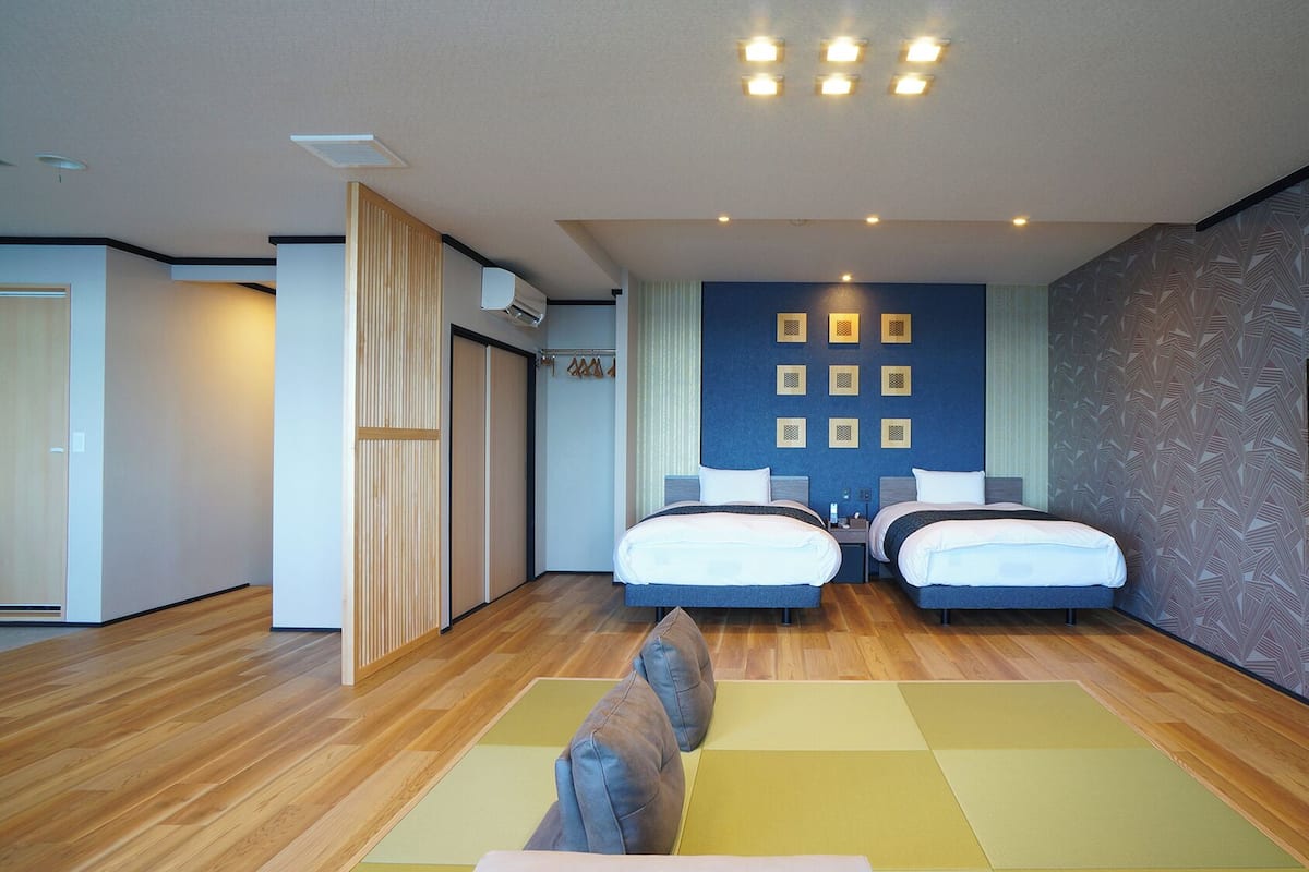 A modern hotel room with two beds, a large mirror, and a wooden floor.