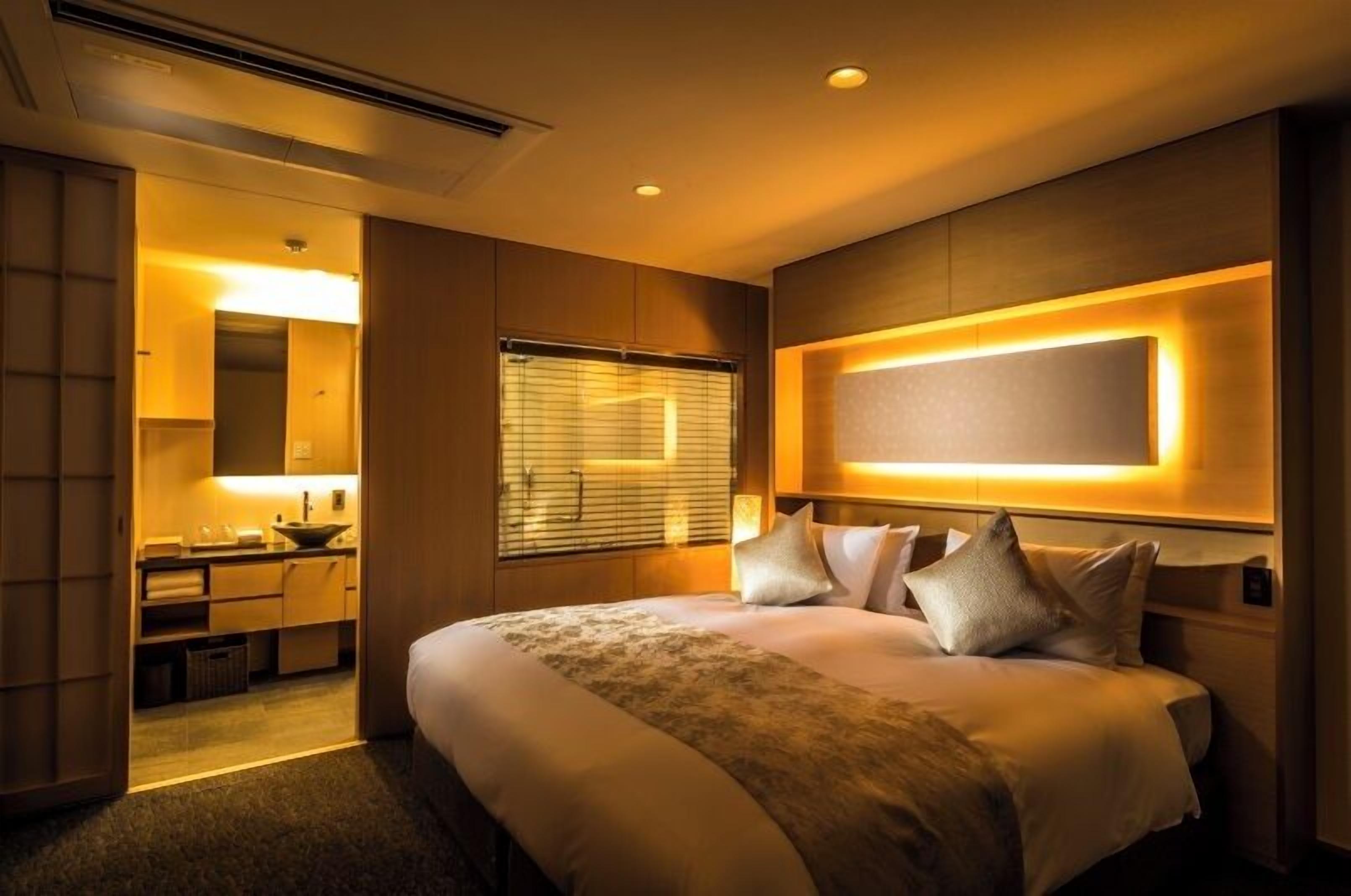 A hotel room with a large bed, a bedside table, a mirror, and a window with blinds.