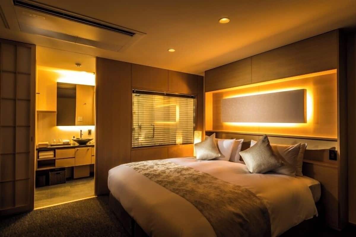 A hotel room with a large bed, a bedside table, a mirror, and a window with blinds.