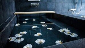 A modern bathroom with dark tiles, a glass shower enclosure, and a wooden bench. - Villa Sanjo Muromachi Kyoto (Kyoto)