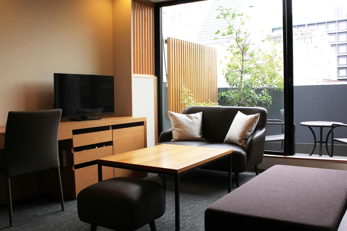 A modern hotel room with a TV, a sofa, a chair, a small table, and a view of the city.