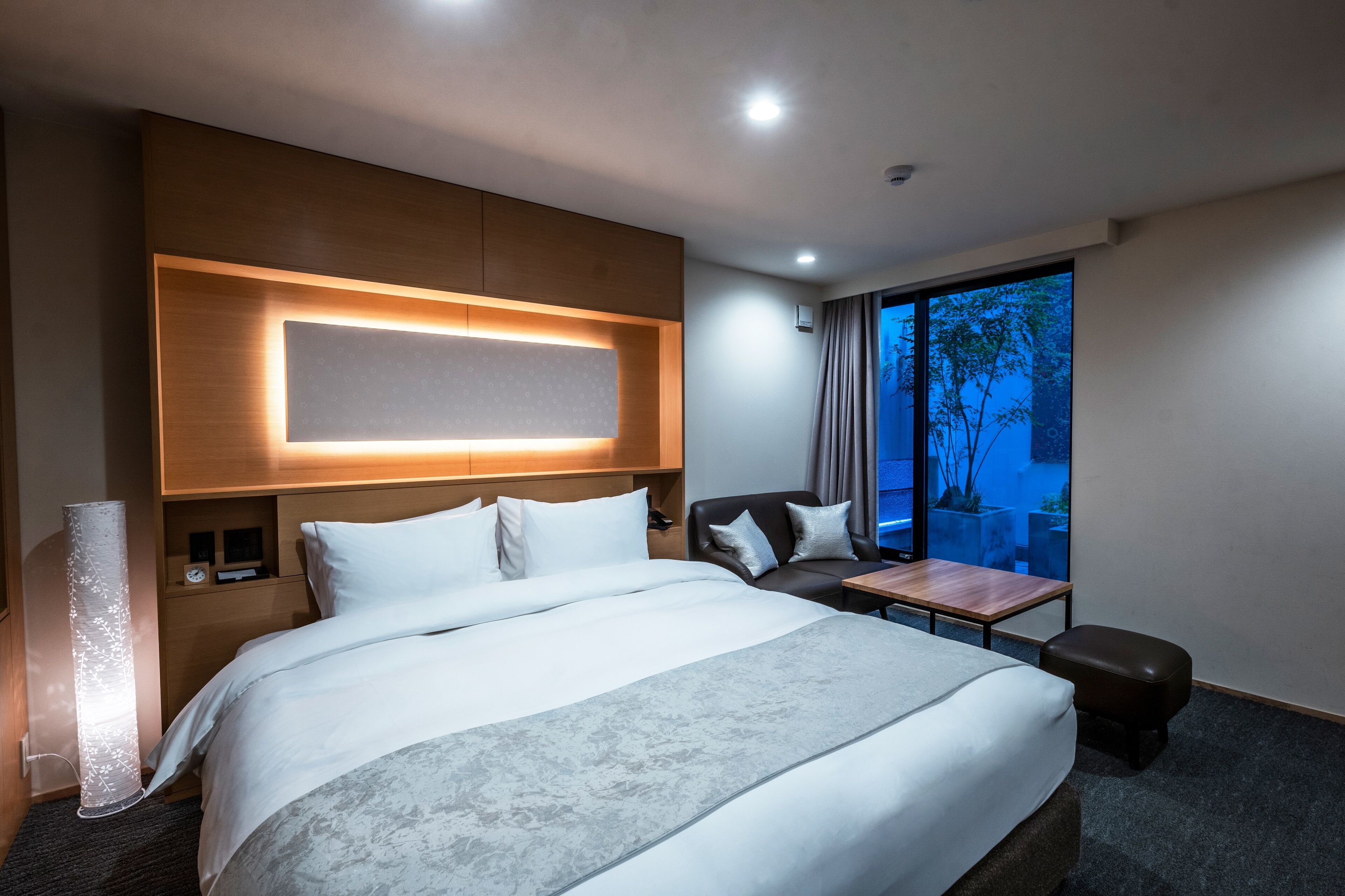 A modern hotel room with a large bed, a desk, and a view of the outdoors.