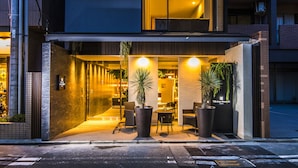 A modern building with a ground-floor entrance, large windows, and outdoor seating area with potted plants.