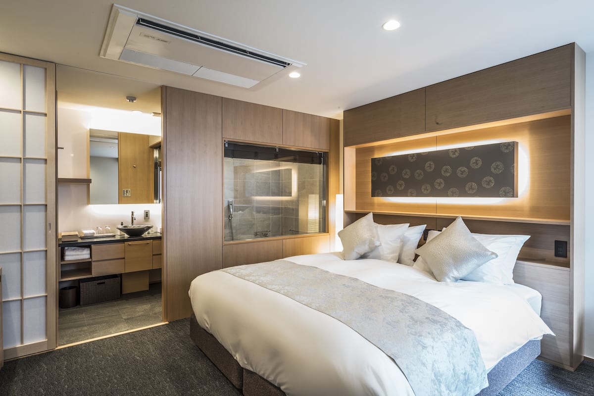 A modern hotel room with a large bed, a built-in vanity, a large mirror, and a unique wall design.