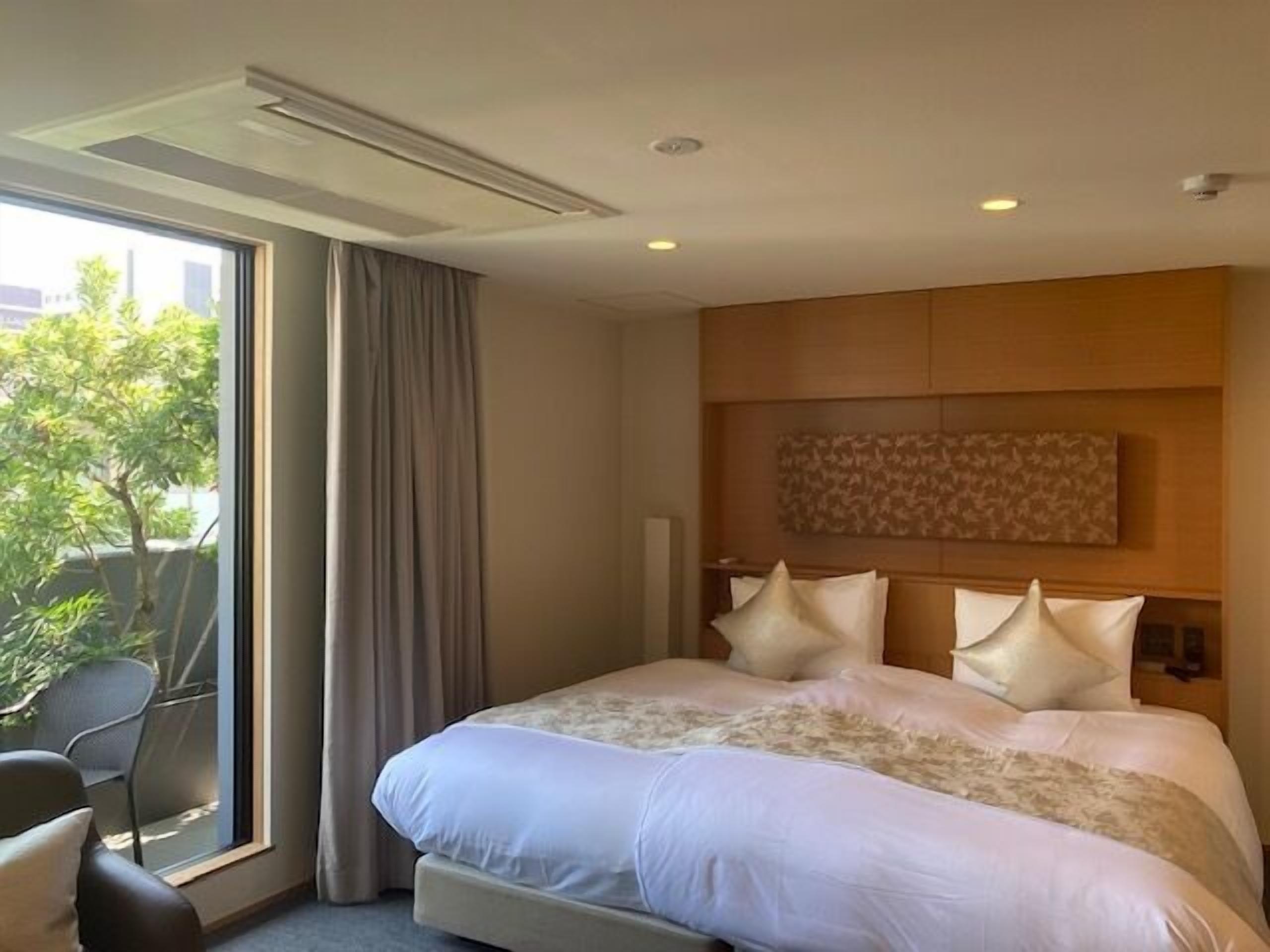 A hotel room with a large bed, a view of greenery outside, and a modern design.