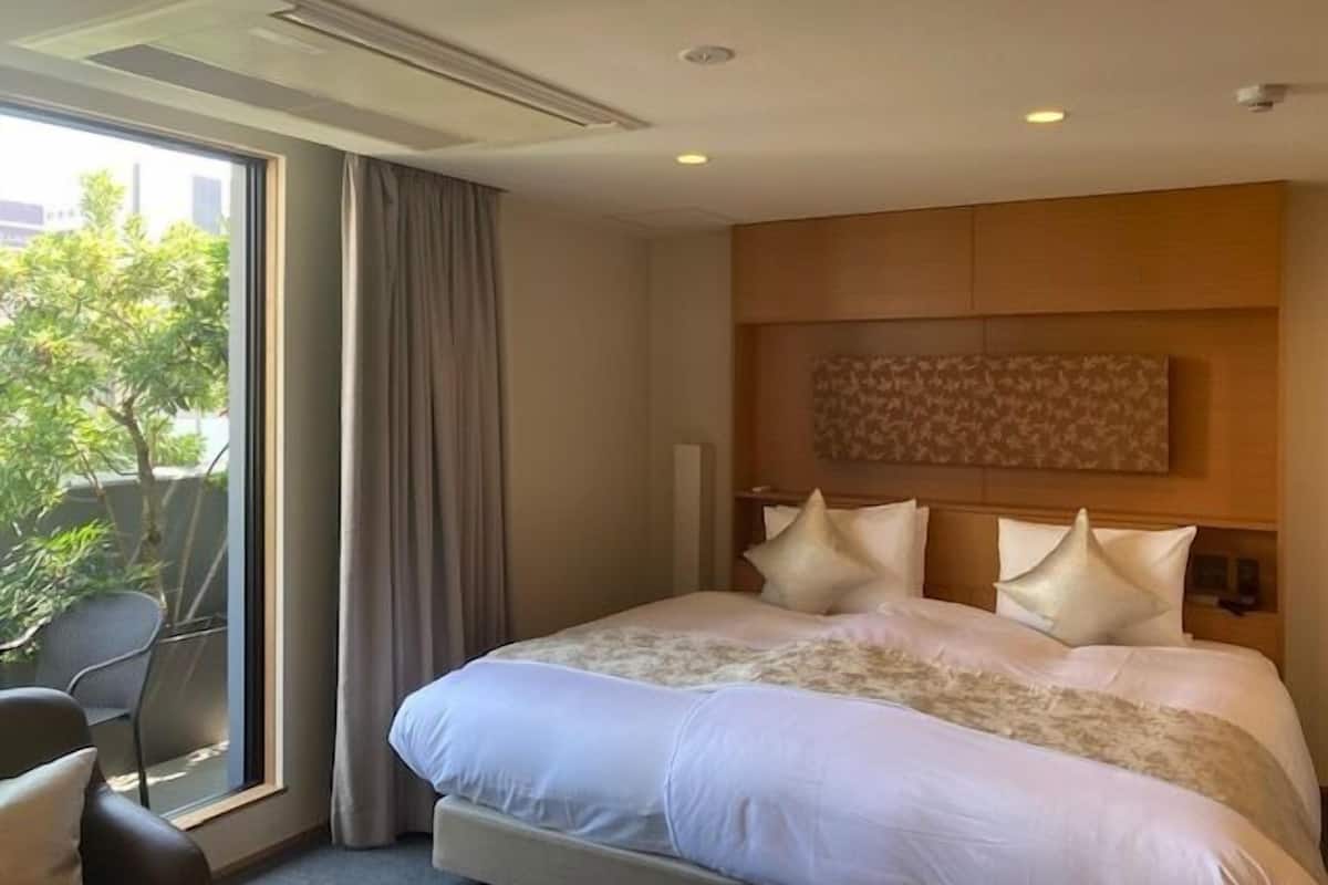 Hotellihuone, jossa on suuri sänky, näkymä vehreään maisemaan ja moderni sisustus.