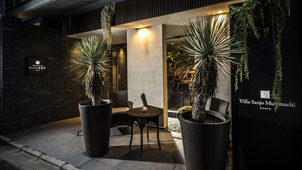A modern hotel entrance with large potted plants, a seating area, and a sign for Villa Sanjo Muramachi in Kyoto.