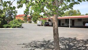 A parking lot with a building that has a red roof and a covered area with tables and chairs. - Copper City Motel (Cobar)