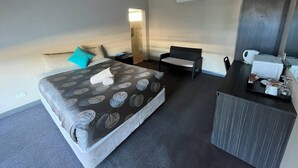 A hotel room with a bed, a desk, a chair, a microwave, and a shower area. - Copper City Motel (Cobar)