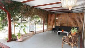 An outdoor seating area with a table and chairs, a potted plant, and a covered section with a lattice wall. - Copper City Motel (Cobar)