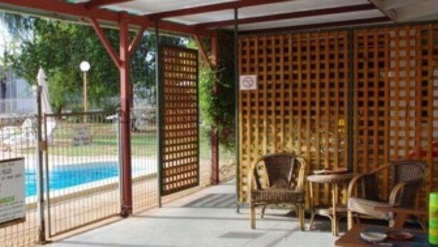 A covered pool area with a fence, chairs, and a table. - Copper City Motel (Cobar)