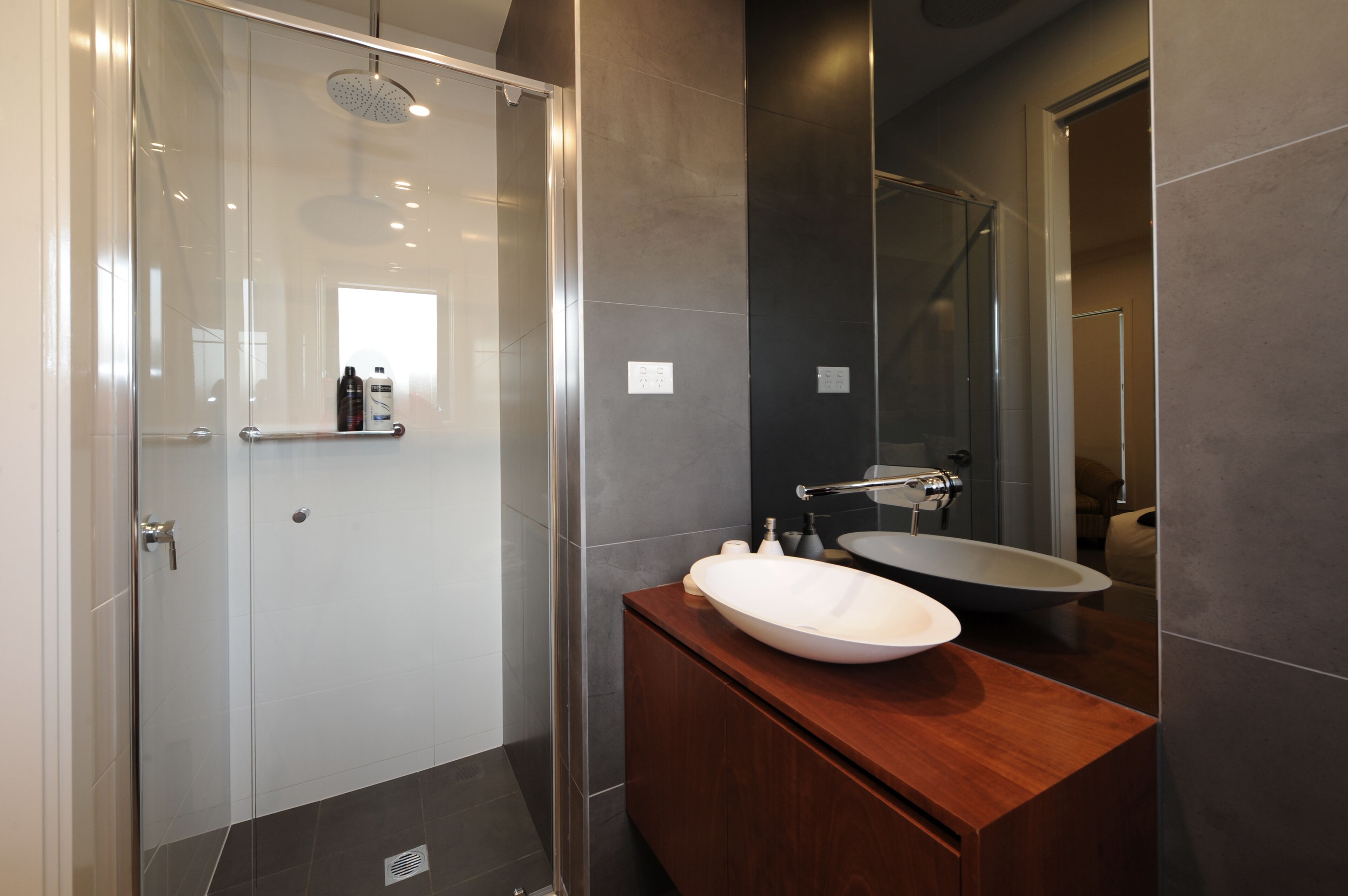 A modern bathroom with a glass shower enclosure, a wooden vanity with a large sink, and a mirror above the sink.