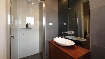 A modern bathroom with a glass shower enclosure, a wooden vanity with a large sink, and a mirror above the sink.