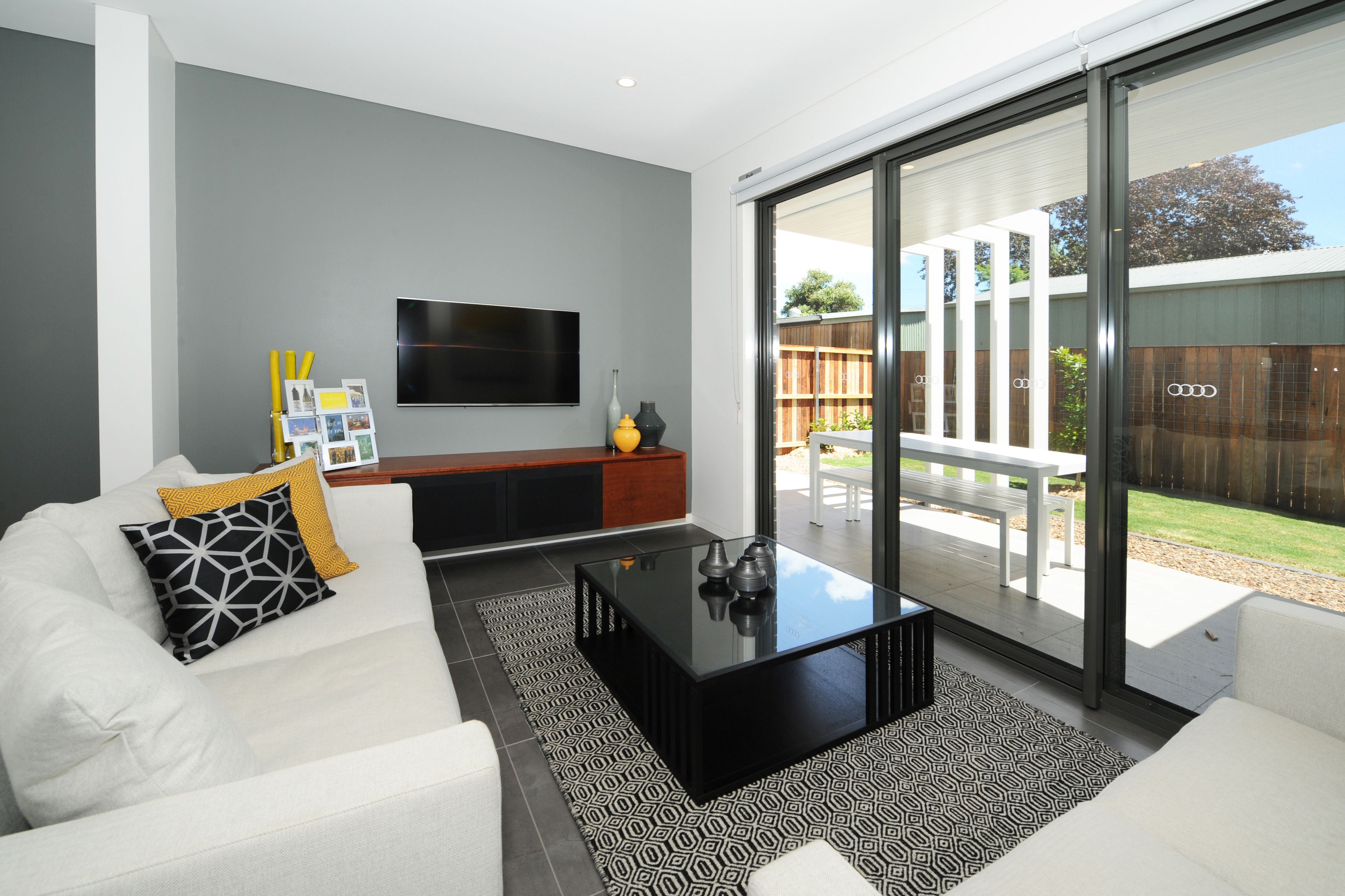 A modern living room with a white sofa, black coffee table, and a flat-screen TV mounted on the wall.