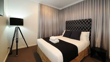 Una cama bien hecha con cabecera blanco y negro, una lámpara sobre un trípode y una mesita de noche.